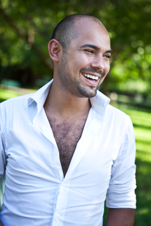 A laughing man in an open white shirt stands in a green garden.
