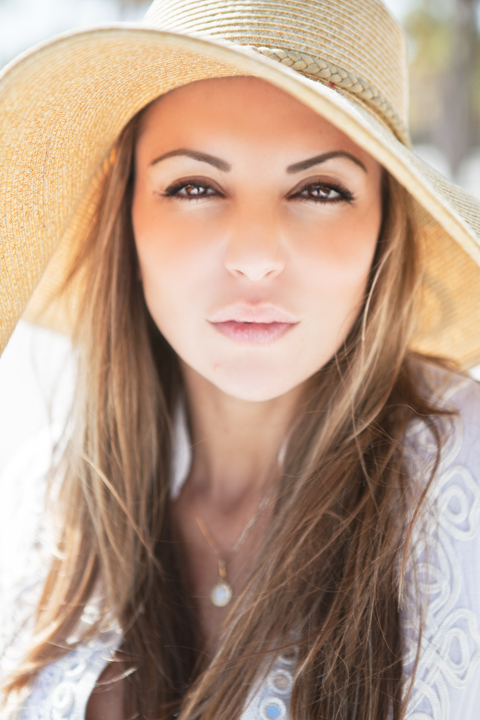 A woman wearing a straw hat looks toward the camera in sunlight.