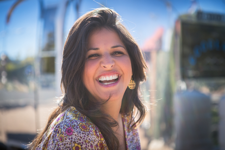 A laughing woman turns toward the camera on a sunny street.