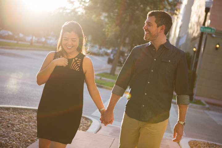 Two adults walk hand in hand along a sunlit city sidewalk.