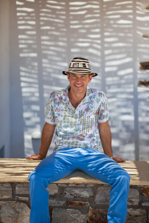 A man in a hat and blue trousers sits beneath patterned shadows.