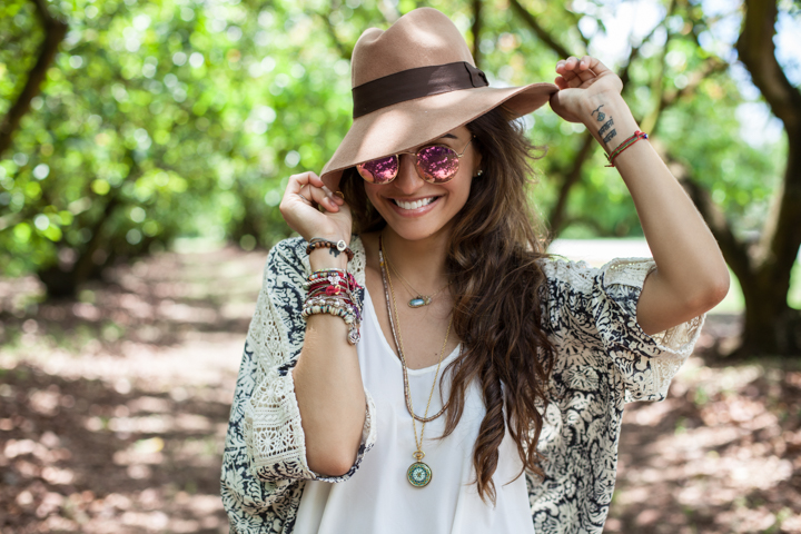 A woman in sunglasses adjusts the brim of her hat in a green garden.