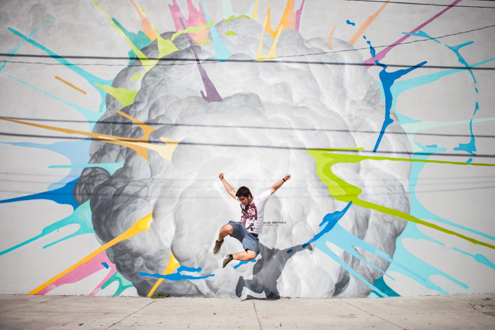 A person jumps with arms spread in front of a colorful abstract mural.