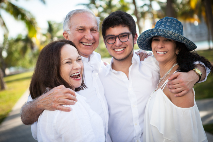 Four smiling adults embrace in an outdoor group portrait.