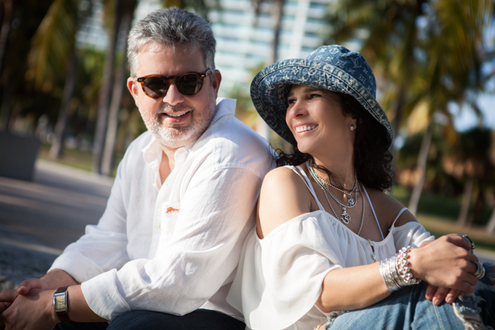 Two adults in sunglasses sit together on a sunny outdoor bench.