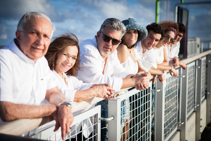 A group of adults leans together along a seaside railing.
