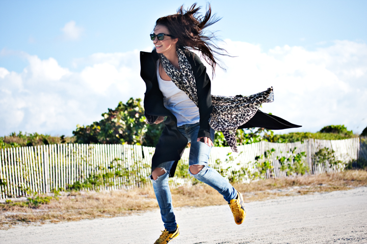 A woman jumps beside a white fence with her hair and patterned jacket flying.