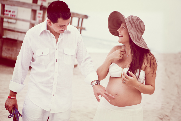 A man holds a pregnant woman's hand on a sunny street.