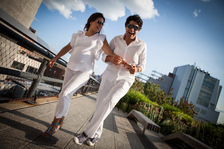 Two adults dressed in white walk hand in hand along a sunny waterfront.