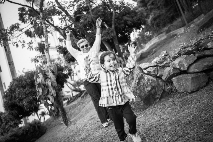 An adult and child raise their arms on a garden swing in black and white.