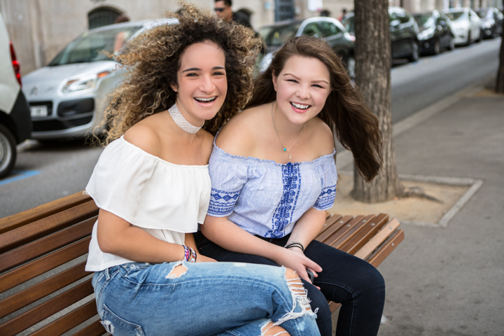 Two laughing women sit close together on a city bench.