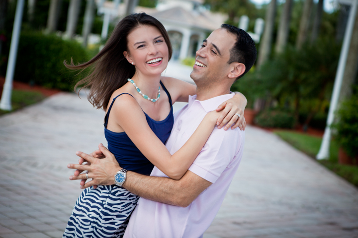 Two adults laugh while embracing on a sunny walkway.