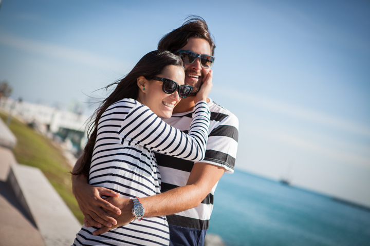 A man hugs a woman from behind beside the sea.