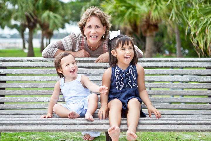 A woman and two children laugh together on a park bench.