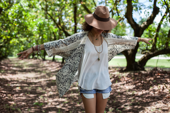 A woman in a hat stretches her arms beneath green garden trees.