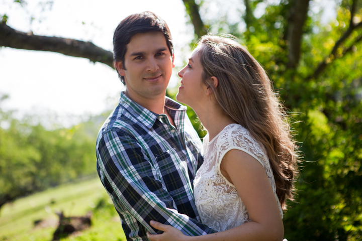 Two adults embrace beneath leafy garden trees.