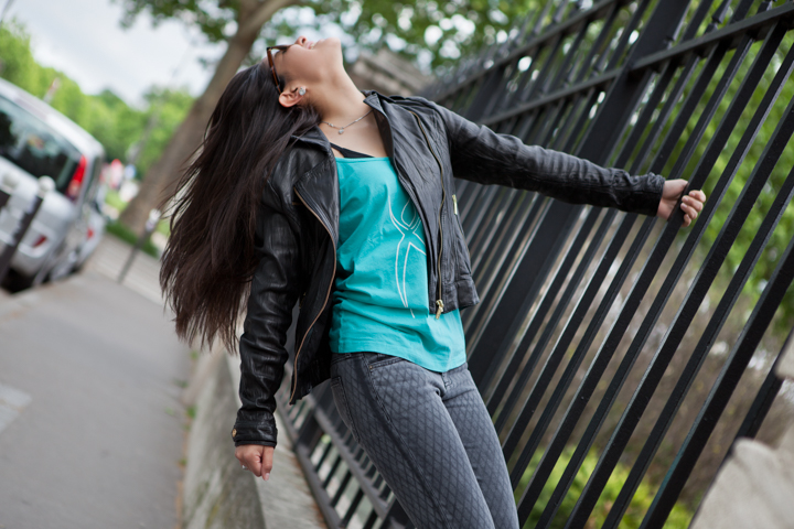 A woman leans back beside a metal fence with her long hair flowing.