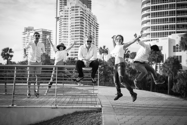 A group jumps together beside a waterfront railing in black and white.