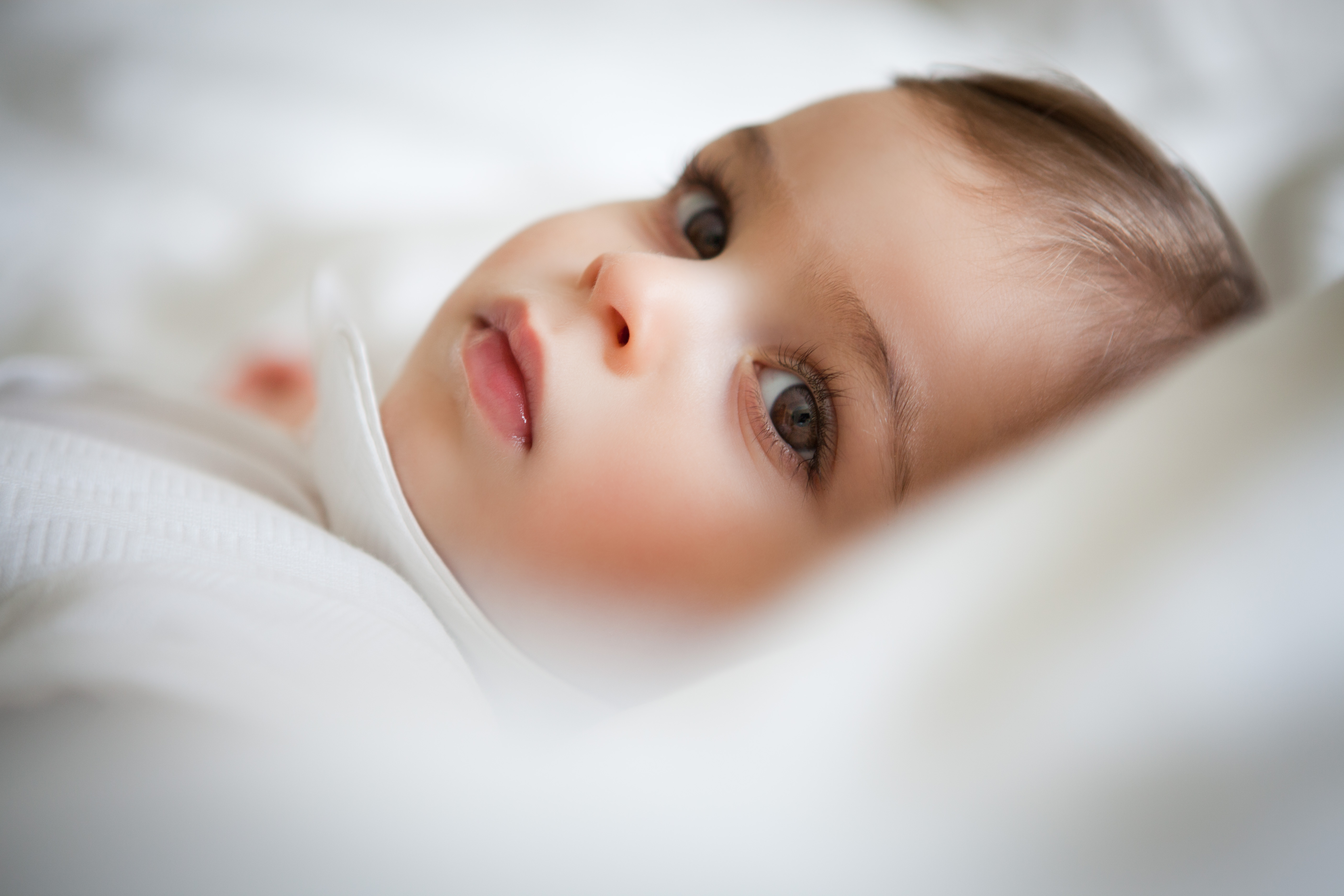 Close-up of a baby resting on white bedding in soft natural light