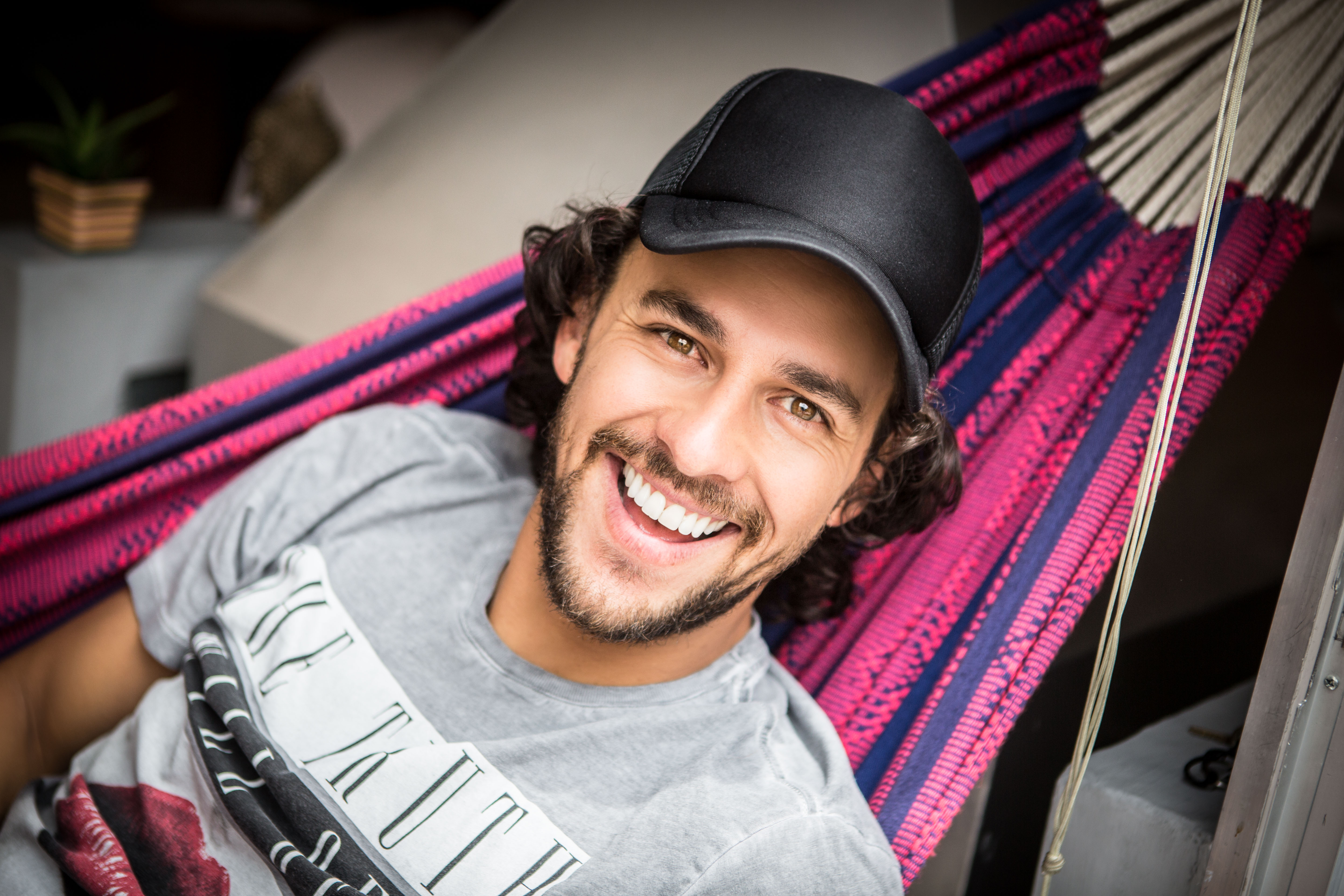 Smiling man wearing a black hat while relaxing in a colorful hammock