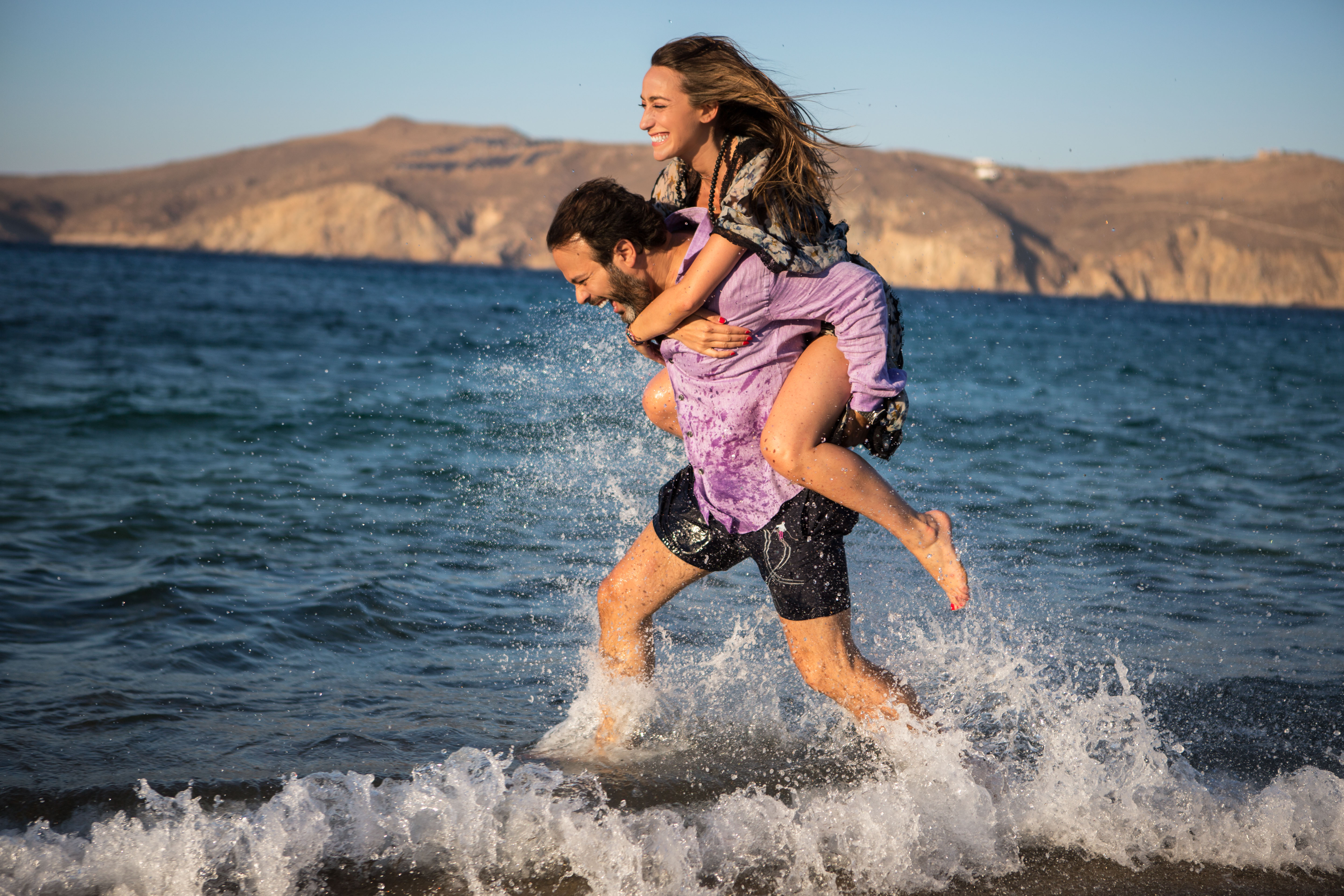Man carrying a woman on his back as they splash through the sea