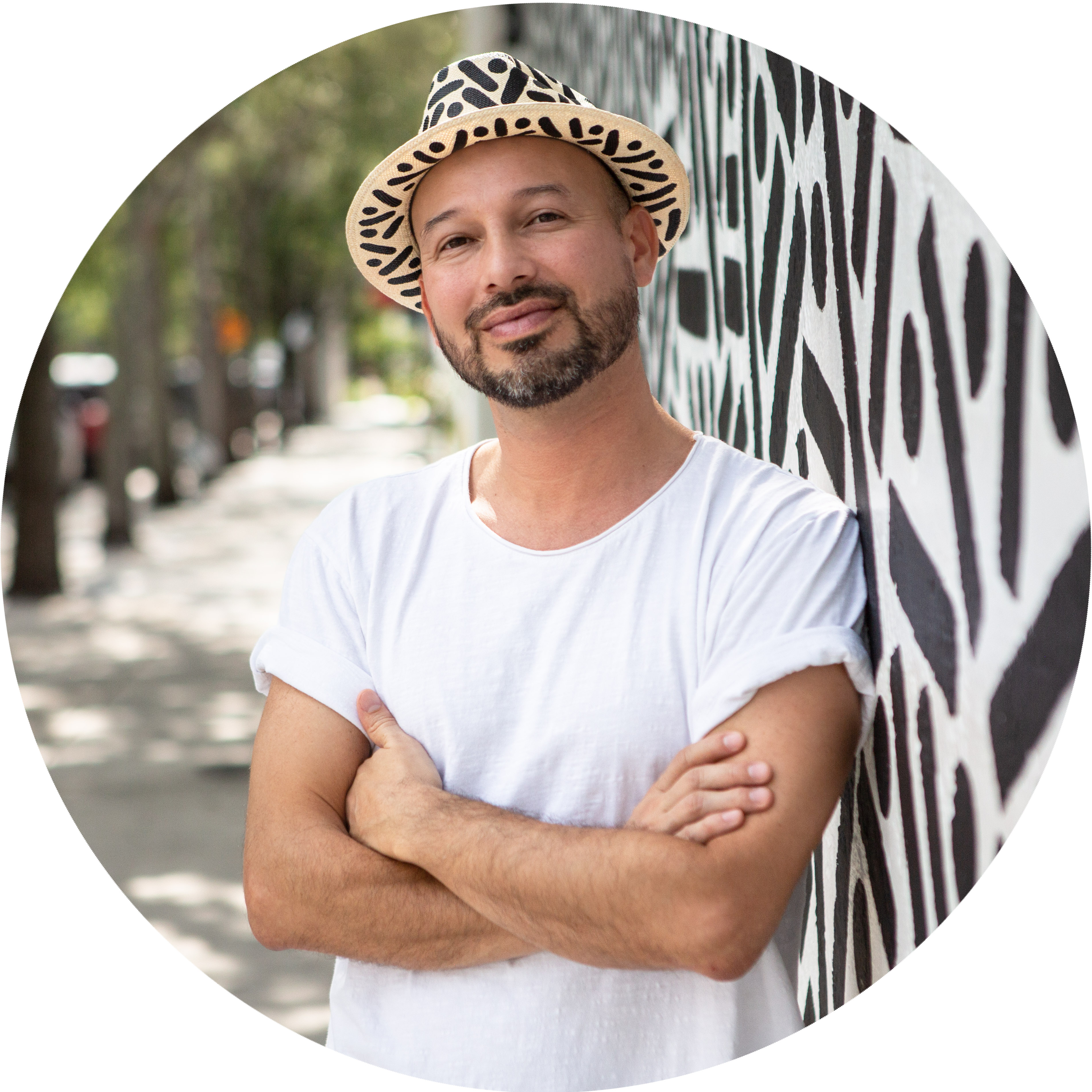 Pipe Yanguas stands beside a black-and-white mural wearing a white shirt and patterned hat.